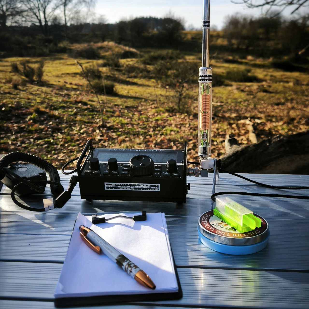 Eine minimalistische portable Funkstation auf einem flachen Felsblock an einem ruhigen Waldsee im Morgengrauen mit dünner Drahtantenne.